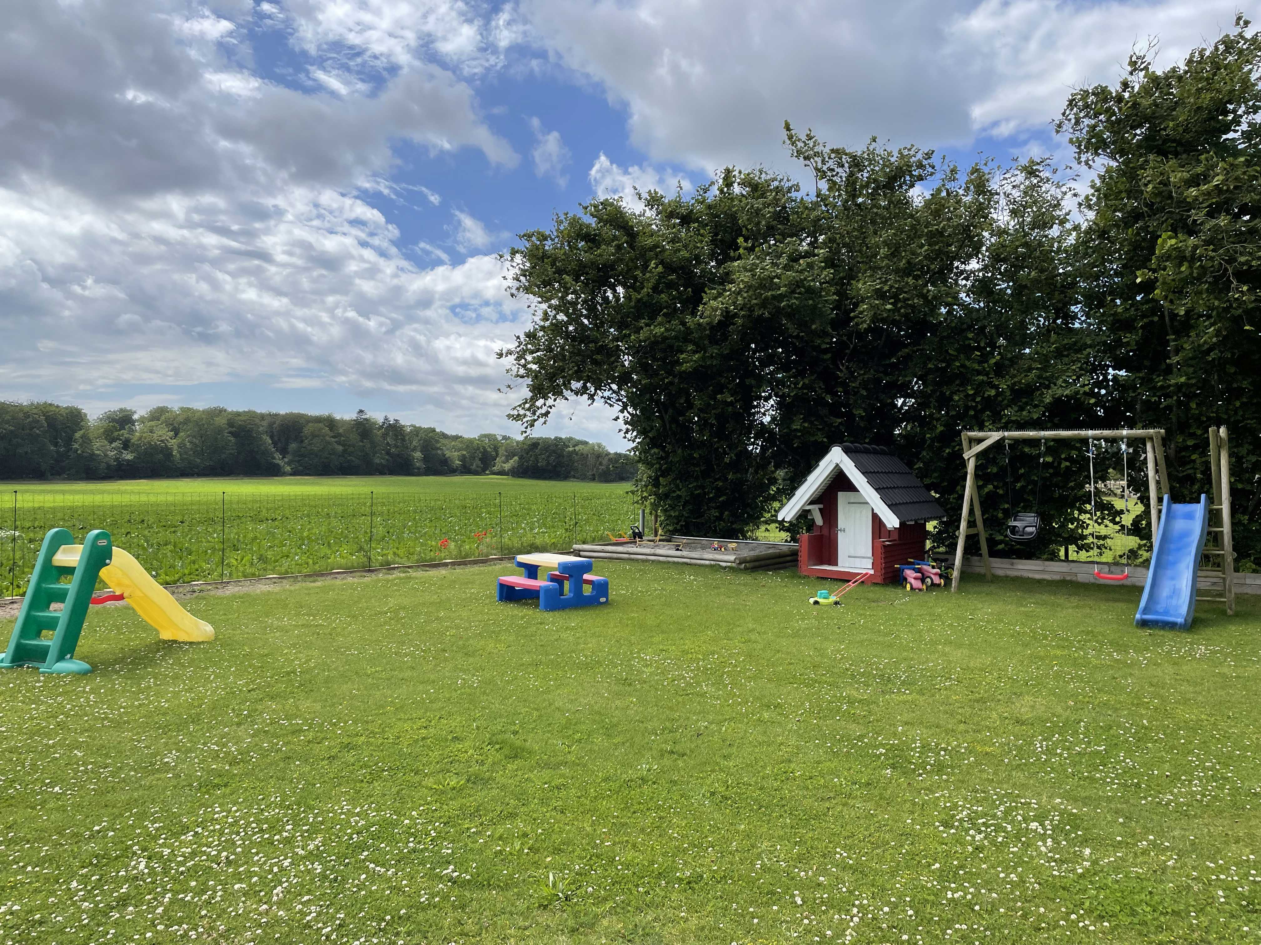 På billedet ses dagplejerens have med sandkasse, gyngestativ, rutsjebane og legehus. Haven er indhegnet.